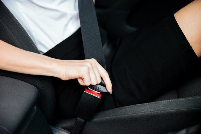 woman sitting in car and putting on her seat belt PH9Q4L3